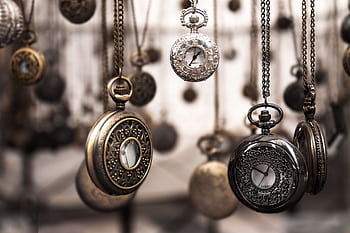 Close-up of antique pocket watches with intricate designs hanging in a blurred vintage setting. HD wallpaper