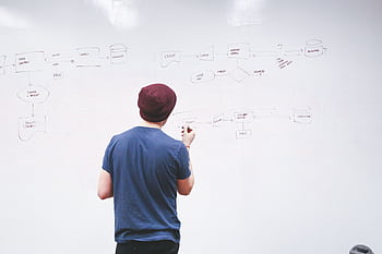 Young man brainstorming and planning a project on a whiteboard with diagrams and notes. HD wallpaper