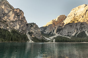 Capture the serene beauty of a reflective lake surrounded by towering mountains and lush forests. HD wallpaper
