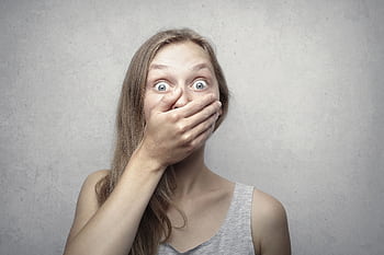A startled woman covers her mouth expressing surprise against a neutral background. HD wallpaper