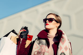 Stylish woman in sunglasses holding shopping bags, embodying modern fashion and luxury lifestyle. HD wallpaper