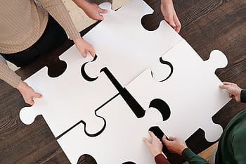 Group collaborating on assembling large puzzle pieces symbolizing teamwork and unity. HD wallpaper