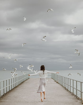 A woman joyfully walking barefoot on a dock surrounded by soaring seagulls, symbolizing dom. HD phone wallpaper