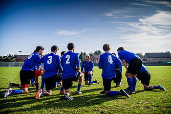 A group of male football players in blue uniforms huddle on a grassy field before a match. HD wallpaper