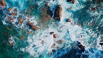Stunning aerial view of ocean waves crashing against rocks, creating a beautiful natural pattern. HD wallpaper