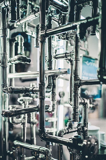 Close-up of complex stainless steel pipes in an industrial setting, showcasing modern engineering. HD phone wallpaper