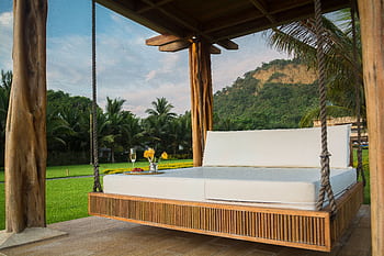 A luxurious swing bed under a wooden canopy with tropical palm trees. HD wallpaper