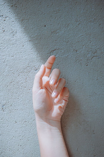 A hand is reaching towards a light against a textured wall, capturing shadows. HD phone wallpaper
