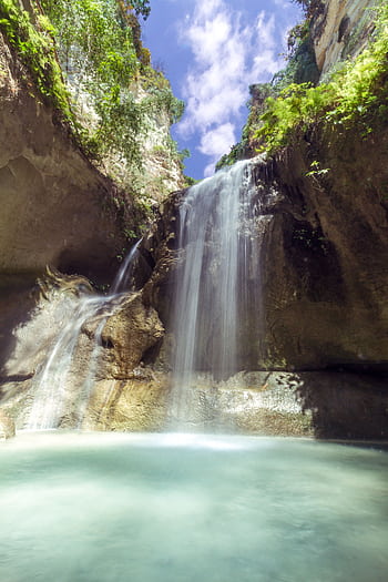 A tranquil waterfall cascading into a serene pool surrounded by lush greenery and rocky cliffs. HD phone wallpaper