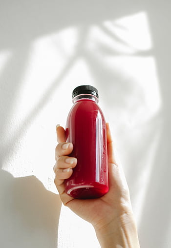 A hand holding a refreshing red juice bottle against a white background, conveying health and freshness. HD phone wallpaper