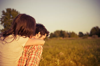 A couple shares a loving embrace during a sunset in a tranquil field. HD wallpaper