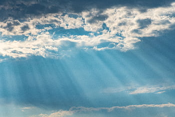 Vibrant sunrays pierce through a cloudy sky, creating a dramatic and dreamy cloudscape. HD wallpaper