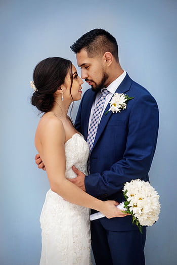 Bride and groom sharing a tender moment with bouquet against a blue background. HD phone wallpaper