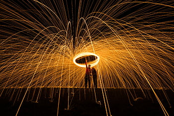 Dramatic long exposure of steel wool light painting with glowing trails and silhouetted figures. HD wallpaper