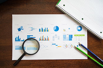 Overhead view of charts and graphs with magnifying glass and stationery on wooden table. HD wallpaper