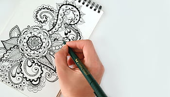 Close-up of a hand drawing an intricate mandala pattern on a sketchbook using a pen. Perfect for creativity themes. HD wallpaper