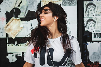 Portrait of a young woman smiling while listening to music with ears against a graffiti wall. HD wallpaper