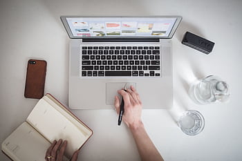Top-down view of a workspace featuring a laptop, notebook, smart, and glass of water, ideal for remote work. HD wallpaper