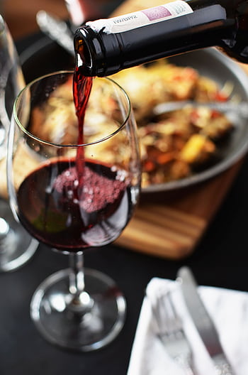 Close-up of red wine being poured into a glass at a romantic dinner setting with food in the background. HD phone wallpaper