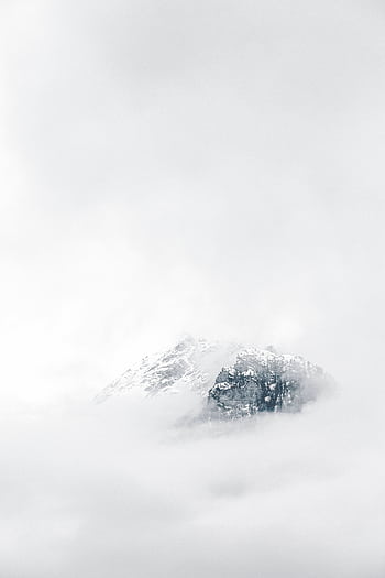 A snow-capped mountain peak emerging through dense fog, creating a serene winter landscape. HD phone wallpaper