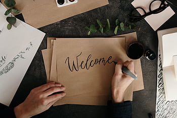 Handwriting a welcome card with calligraphy on craft paper, surrounded by art supplies. HD wallpaper