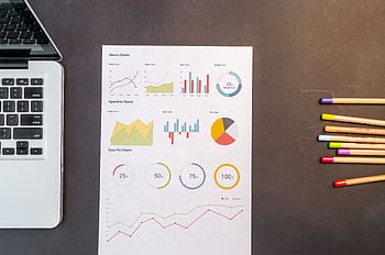 Top view of charts and colored pencils on a desk next to a laptop, perfect for business or education themes. HD wallpaper