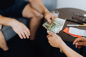 Close-up of hands exchanging US dollar bills, symbolizing a financial transaction or payment. HD wallpaper