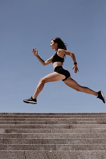 Energetic woman in active wear jumping on stairs outdoors, showcasing fitness and determination. HD phone wallpaper
