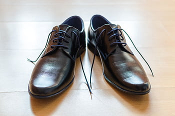 A pair of shiny, elegant black leather dress shoes with laces on a wooden floor. HD wallpaper