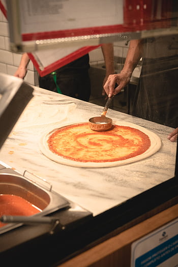 Authentic Italian pizza preparation with fresh tomato sauce on dough in a Brazilian kitchen. HD phone wallpaper