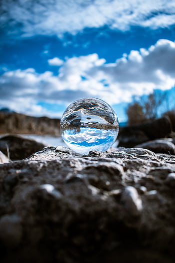 A crystal ball reflecting the sky and clouds creates a mesmerizing scene on rough terrain. HD phone wallpaper