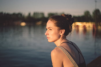A thoughtful woman gazing over a calm lake during sunset, capturing serenity and contemplation. HD wallpaper