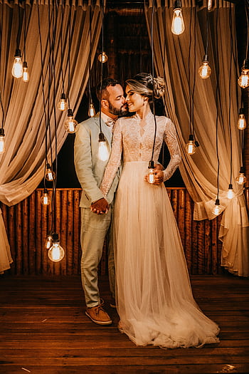 Bride and groom hold hands under hanging lights in an elegant indoor setting. HD phone wallpaper