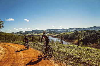 Two cyclists riding on a dirt trail with stunning mountain views and clear skies. HD wallpaper