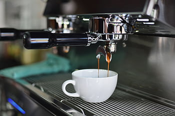 Close-up of espresso pouring from a shiny coffee machine into a white cup, perfect for lovers of caffeine and barista art. HD wallpaper