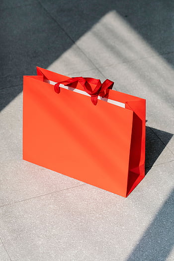 Bright red shopping bag with sunlit shadows on a tiled floor, symbolizing retail and commerce. HD phone wallpaper