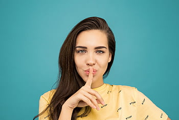 Portrait of a woman with brown hair posing with a hush gesture against a blue background. HD wallpaper