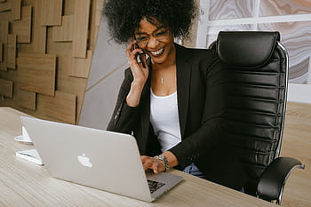 Smiling woman on call while working on a laptop in a stylish office. HD wallpaper