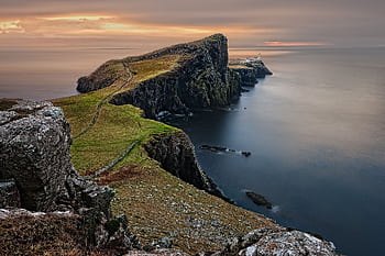A stunning sunset view of Neist Point Lighthouse with cliffs and serene sea in Scotland. HD wallpaper