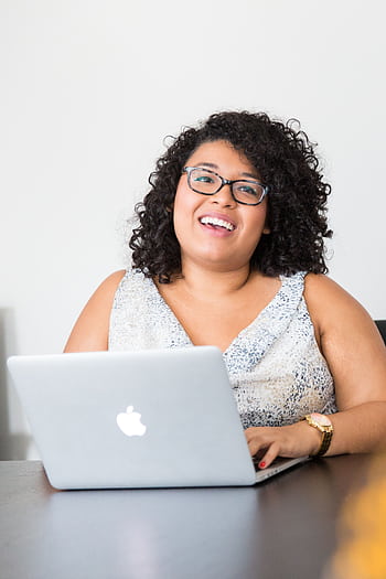Happy businesswoman with curly hair using a laptop at her desk, smiling confidently. HD phone wallpaper
