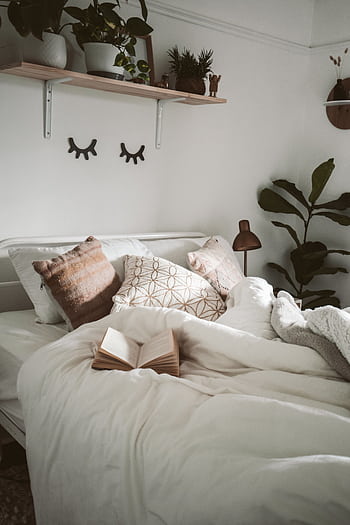 Warm and inviting bedroom setup with decorative pillows, plants, and an open book for a cozy ambiance. HD phone wallpaper