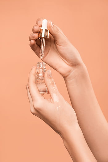 Close-up of hands using a dropper to apply skincare serum, ideal for health and beauty content. HD phone wallpaper