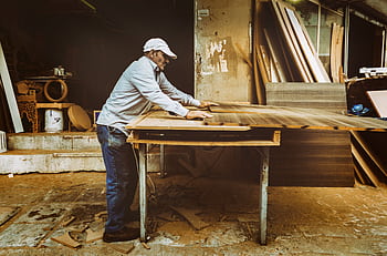 Carpenter focuses on woodworking project inside a busy workshop, surrounded by materials. HD wallpaper