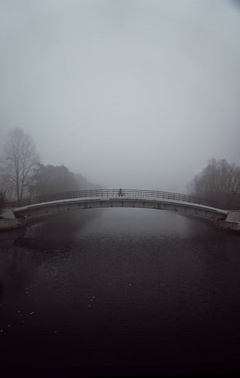 A lone person crosses a foggy bridge over a calm river, enveloped in mist and tranquility. HD phone wallpaper