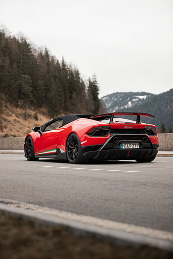 Red luxury sports car parked on a scenic mountain road with a forested backdrop. HD phone wallpaper