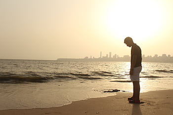 A young man stands alone on an Indian beach, silhouetted against a sunset skyline. HD wallpaper