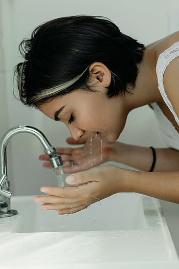 A woman with short hair gently washes her face at a bathroom sink, embracing a clean and refreshing start to the day. HD phone wallpaper