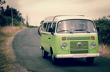 Classic green Volkswagen campervan driving on a quiet country road, perfect for road trips and adventure in nature. HD wallpaper