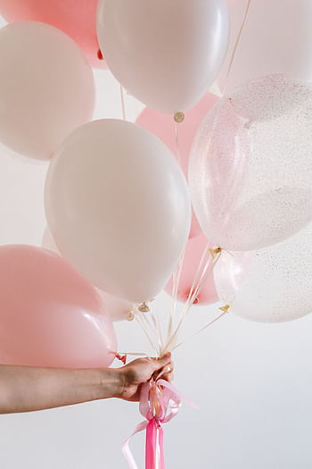 A pastel pink and white balloon bouquet held by a hand against a light background, ideal for celebrations. HD phone wallpaper