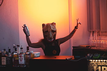A bartender in a mask mixes drinks at an indoor party with a warm glow. HD wallpaper